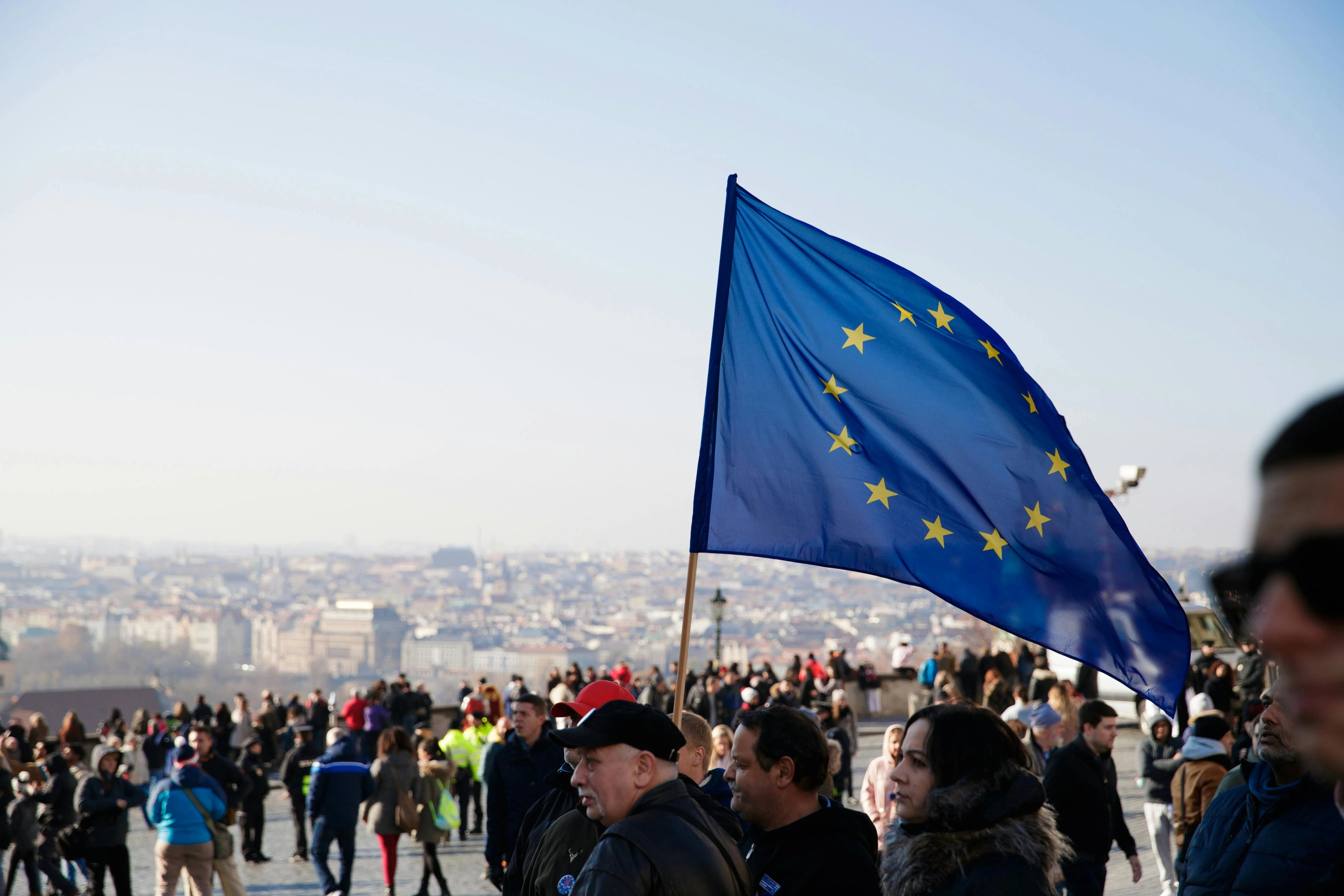 Person holding a European Union flag in a crowd with a cityscape in the background